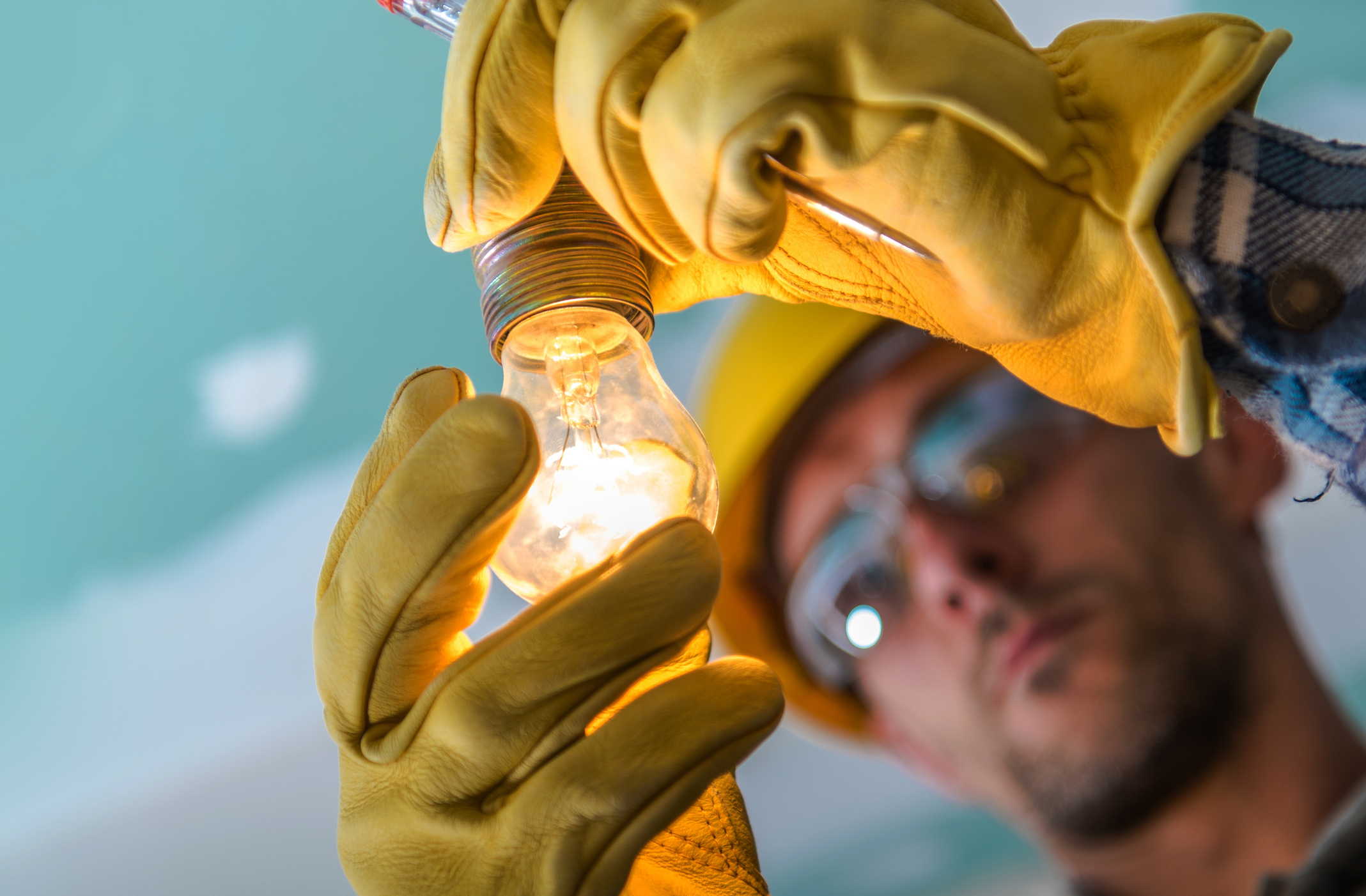 Close up of gloved hands holding a lit light bulb.