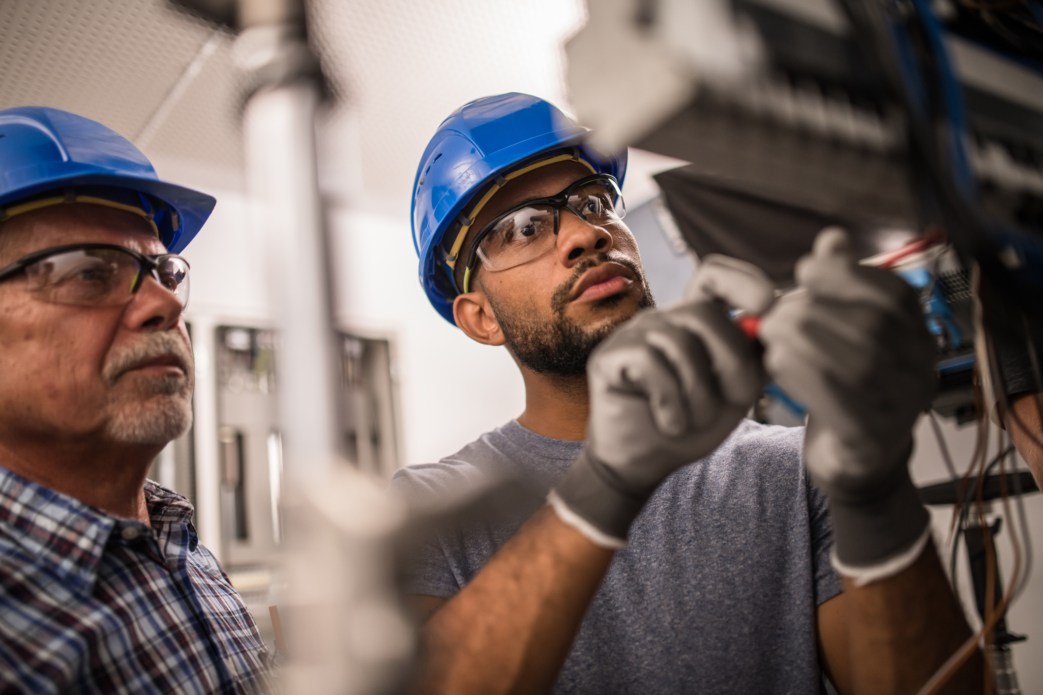 Two electricians work together at a fuse box.