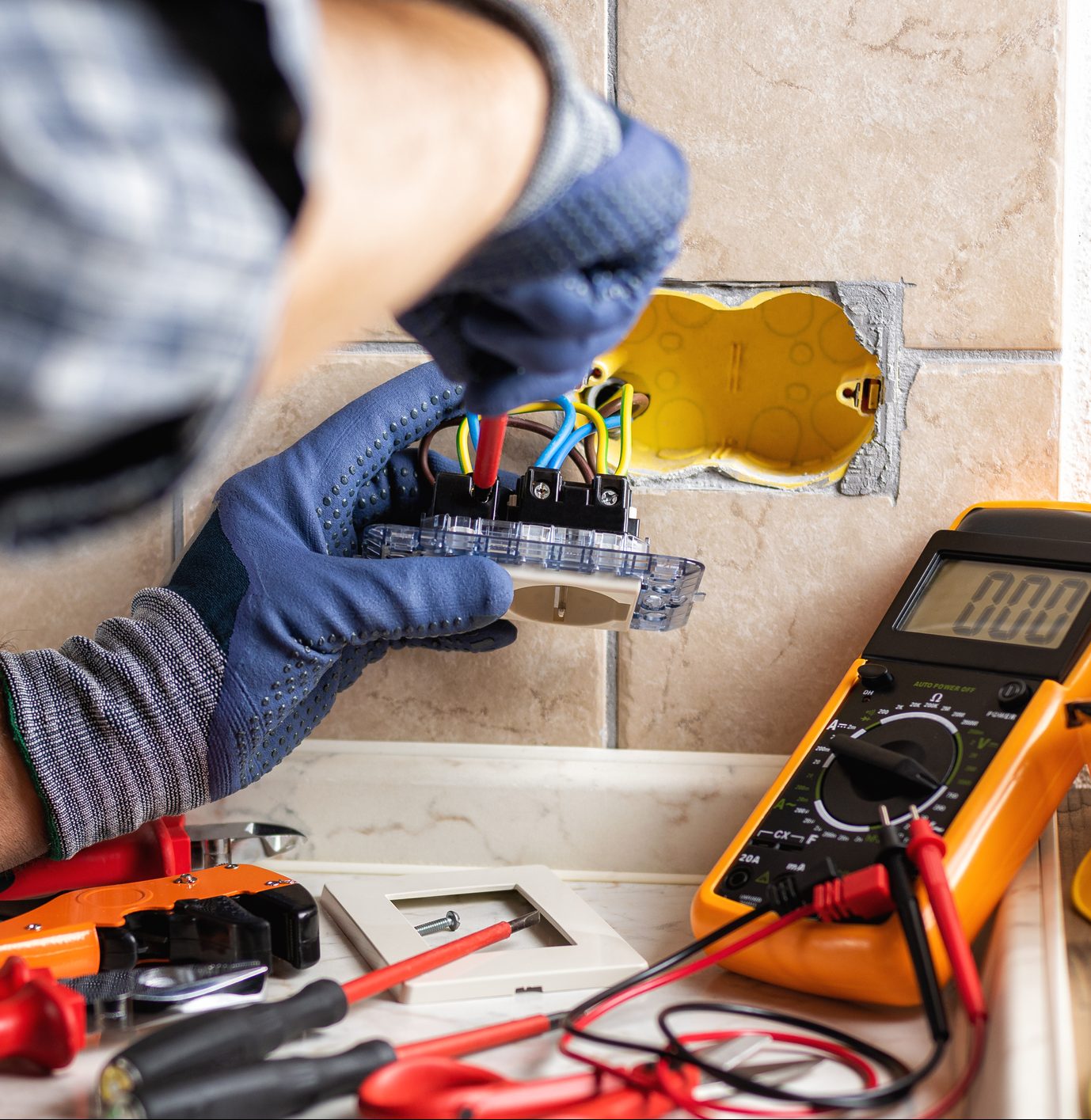 Electrician works on an electrical socket with a screwdriver.